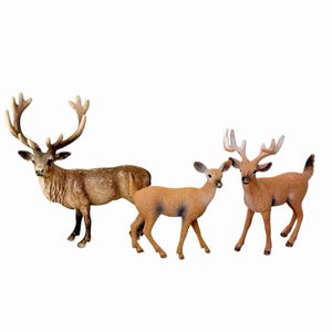 Könnte beinhalten: Ein Set aus drei Hirschfiguren, bestehend aus einem großen Hirsch mit ausgeprägtem Geweih, einem kleineren Reh und einem jungen Hirsch mit kleinerem Geweih. Die Figuren sind in Braun- und Beigetönen gehalten und haben eine Fellstruktur.