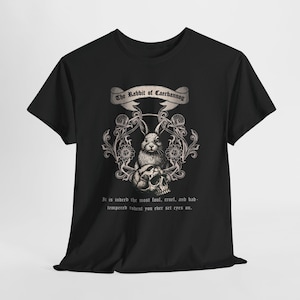 Könnte beinhalten: Schwarzes T-Shirt mit einer detaillierten Illustration eines Kaninchens über einem Totenkopf, mit floralen Akzenten und dem Text "The Rabbit of Caerbannog". Unter dem Bild steht der Text "It is indeed the most foul, cruel, and bad-tempered rodent you ever set eyes on."