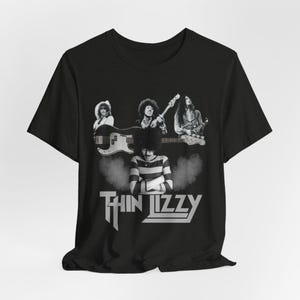 May include: Black t-shirt featuring a black and white image of the band Thin Lizzy. The image includes the band members with their instruments and the band's logo in white.