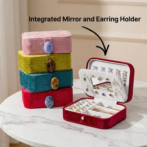 May include: A stack of four velvet jewelry boxes in pink, yellow-green, teal, and red, each with a gemstone clasp. The open red box reveals a mirror, earring holders, and compartments for rings and necklaces. Text: Integrated Mirror and Earring Holder.