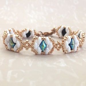 Op de afbeelding: Een witte en gouden kralen armband met iriserende blauwe en groene diamantvormige kralen.