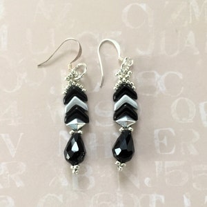 May include: A pair of silver dangle earrings with black and silver chevron-shaped beads and a black teardrop-shaped bead at the bottom.