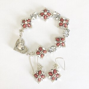 May include: A silver bracelet and earrings set with red and silver bead accents. The bracelet has a heart-shaped clasp. The earrings are dangle style.