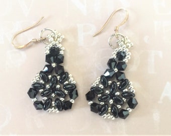 May include: A pair of black and silver beaded dangle earrings with a teardrop shape. The earrings are made with small black beads and silver beads, and they have a delicate, intricate design.
