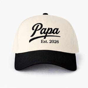 Pode incluir: Boné de beisebol creme com aba preta. A palavra "Papa" é bordada em preto na frente, com "Est. 2026" abaixo. O boné tem uma aba curva e um botão na parte superior.