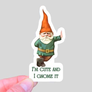 May include: A sticker featuring a garden gnome with a red hat, green tunic, and a white beard. The gnome is giving a hand gesture. Text on the sticker reads, "I'm cute and I gnome it."