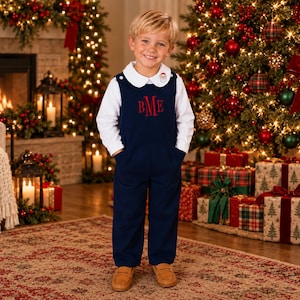 May include: A navy blue overall with red embroidered monogram letters BME on the chest, worn over a white long-sleeve shirt with a rounded collar featuring a small Santa Claus embroidery detail on the right side of the collar.