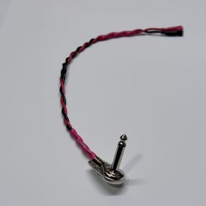 May include: A silver-colored instrument cable with a black and pink twisted wire and a silver-colored plug. The cable is designed for connecting musical instruments to amplifiers or other audio equipment.