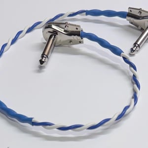 Puede incluir: Cable de instrumento corto en ángulo recto con conectores plateados y un cable trenzado azul y blanco. Diseñado para conectar instrumentos musicales o equipos de audio.