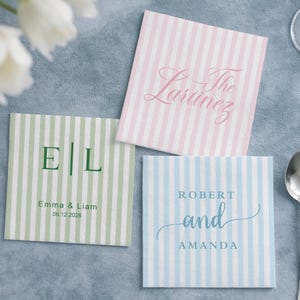 May include: Three square coasters with vertical stripes in pastel colours. One is green with initials and a date, another is pink with a script name, and the third is blue with names.
