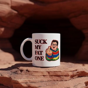 Könnte beinhalten: Weiße Keramik-Tasse mit dem Text "SUCK MY FAT ONE" in Burgunderrot. Die Tasse zeigt eine Cartoon-Illustration einer Person, die den Mittelfinger zeigt. Die Person trägt eine Brille und einen gestreiften Pullover.