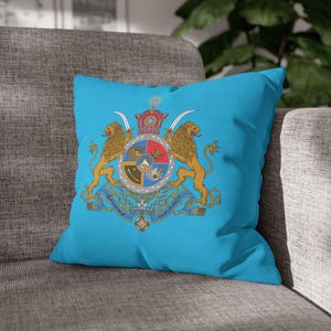 May include: A square, turquoise cushion displaying a detailed coat of arms. Two golden lions flank a central shield, topped with a crown and curved swords. The design includes intricate details in red, gold, and blue.