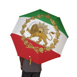 Puede incluir: Un paraguas abierto con el diseño de la bandera iraní. El paraguas tiene un esquema de color rojo, blanco y verde. La sección blanca muestra un león dorado sosteniendo una espada, rodeado por una corona y un sol radiante.