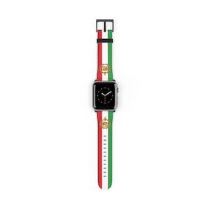 Puede incluir: Un reloj inteligente negro con una correa con un diseño de rayas rojas, blancas y verdes. La correa incluye un emblema dorado. El reloj se muestra sobre un fondo blanco.