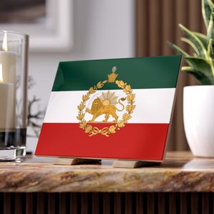 Peut inclure: Carreau carré décoratif représentant le drapeau iranien, avec un schéma de couleurs vert, blanc et rouge. Le centre affiche un emblème doré d'un lion et d'un soleil dans une couronne. Le carreau est soutenu par deux petits supports en bois.