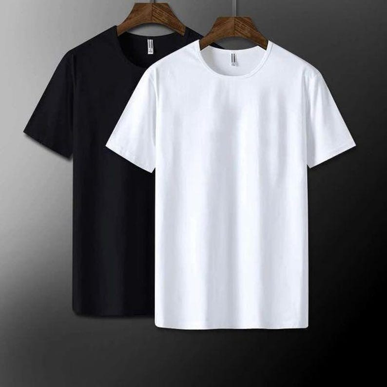 May include: Two short-sleeved t-shirts, one black and one white, hanging on wooden hangers. The shirts have a simple, classic design with a crew neck. The background is a gradient of dark gray to black.
