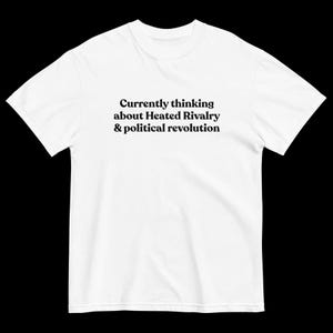 May include: White t-shirt with the text "Currently thinking about Heated Rivalry & political revolution" in black. The shirt is a short-sleeved crew neck.