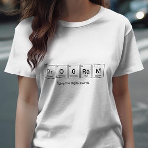 May include: White t-shirt with the word "PROGRAM" spelled out using a periodic table design. The text "Solve the Digital Puzzle" is below the word. The shirt is a casual wear item.