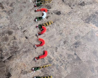 May include: A collection of colorful fishing lures arranged vertically. The lures feature various designs with red, yellow, green, and white accents. Each lure has a small hook and is designed to attract fish.