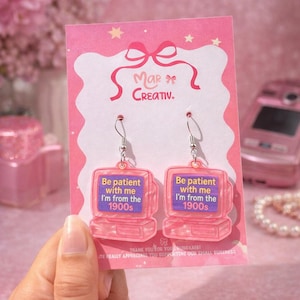 May include: Pink acrylic earrings shaped like retro computers, with the text "Be patient with me I'm from the 1900s" on the screen. The earrings are on a pink card with the brand name "Mar Creativ."