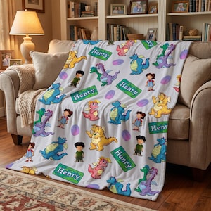 May include: A white fleece blanket featuring a repeating pattern of cartoon dragons in blue, yellow, green, and pink, along with illustrations of two children and green rectangular name tags with the name Henry printed in white text.