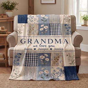 May include: A cream-colored patchwork blanket with blue floral and gingham patterns. The blanket has the word "GRANDMA" in navy blue, along with the phrase "we love you" and the names Justin, Juniper, and Jessica.