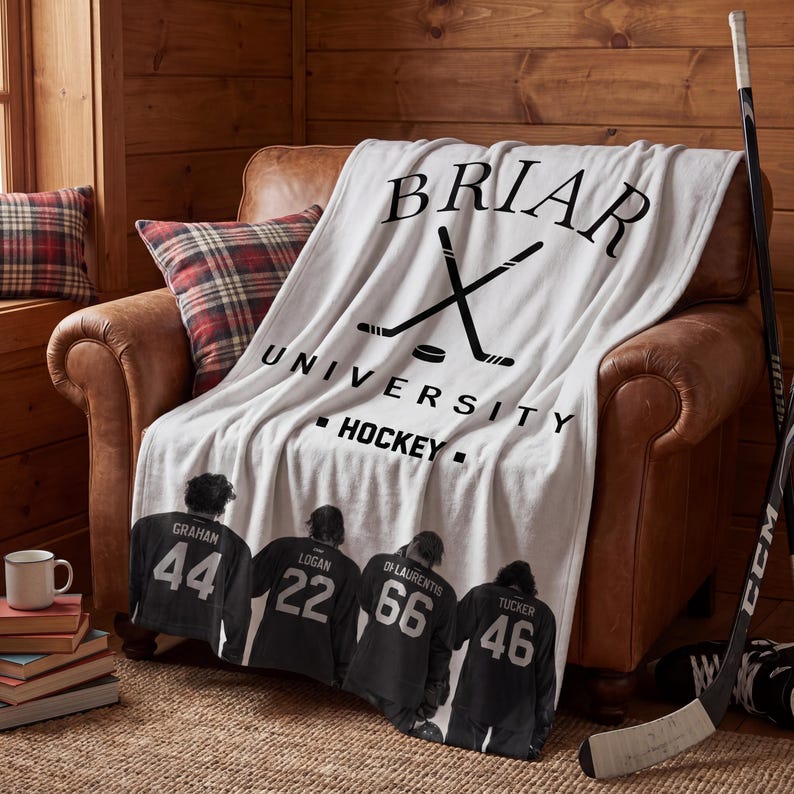 Pu&ograve; includere: Una coperta in pile bianca con il testo nero BRIAR UNIVERSITY HOCKEY e un grafico di bastoni da hockey incrociati. La parte inferiore mostra quattro giocatori di hockey con maglie nere con i nomi GRAHAM 44, LOGAN 22, DI LAURENTIS 66 e TUCKER 46.