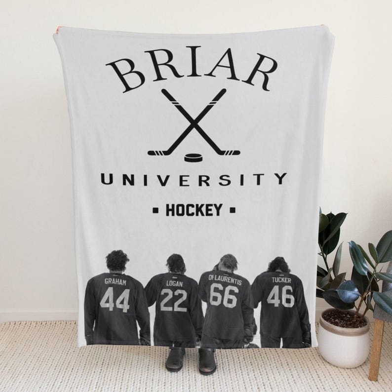 Pu&ograve; includere: Una coperta in pile bianca con una grafica nera di due bastoni da hockey incrociati e un disco. Il testo recita BRIAR UNIVERSITY HOCKEY. Sotto, quattro giocatori di hockey in maglie scure con nomi e i numeri 44, 22, 66 e 46 sono raffigurati.