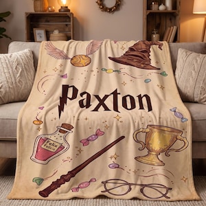May include: A beige fleece blanket featuring the name Paxton in dark brown lettering with a lightning bolt. The design includes illustrations of a golden snitch, a brown sorting hat, a potion bottle labeled Felix Felicis, a wand, a gold cup, and glasses.