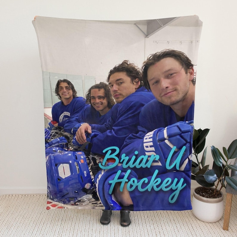 Pu&ograve; includere: Una coperta rettangolare in pile con una fotografia stampata di quattro persone che indossano maglie ed equipaggiamento da hockey blu. Il testo "Briar U Hockey" &egrave; stampato in un carattere corsivo azzurro nella parte inferiore della coperta.