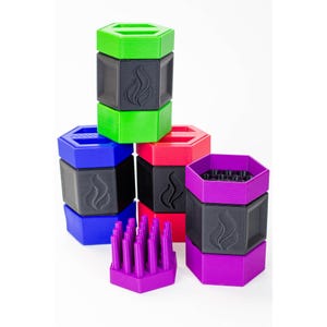 May include: A collection of colorful, hexagonal containers in green, blue, red, and purple. Each container has a black center with a flame design. One purple container is open, revealing a set of purple pegs. The containers are stacked and arranged against a white background.