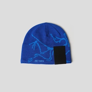 May include: A blue beanie with a light blue graphic design and a black tag. The beanie features the brand name "Arc'teryx" in white text. The hat is made of a soft, knitted material.