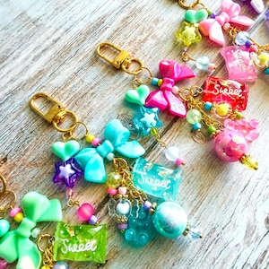May include: Colorful keychains with gold-tone clasps. Each keychain features a variety of charms, including bows, stars, and candy-shaped pieces. Some charms have the word "Sweet" on them. The keychains are adorned with beads in various colors.