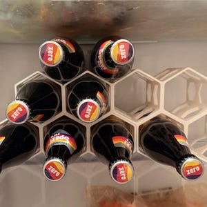 May include: A white hexagonal wine rack holding several dark glass bottles with colorful labels and the word "Zero" on the bottle caps. The bottles are arranged in a refrigerator.