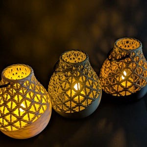 May include: Three decorative lanterns with a geometric woven pattern. The lanterns have a warm, yellow glow emanating from within. The bases are a light beige color, and the tops are a darker beige.