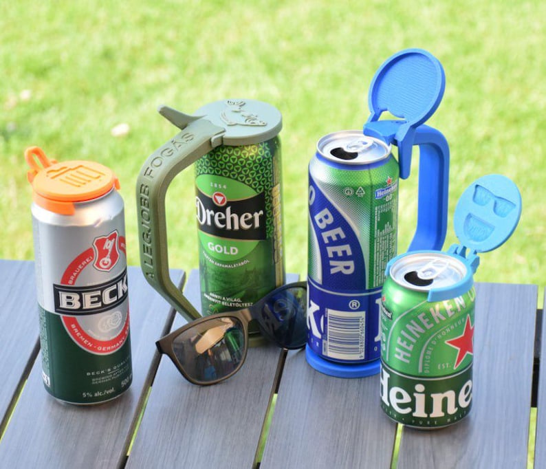 May include: An assortment of beer cans with colorful can toppers and a pair of sunglasses on a wooden table. The cans include Beck's, Dreher Gold, and Heineken. The can toppers are orange, blue, and green.