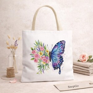 May include: White canvas tote bag with a watercolor design of a blue and purple butterfly and a bouquet of pink, yellow, and purple flowers. The bag has beige handles and the text "SnepGo" on a tag.