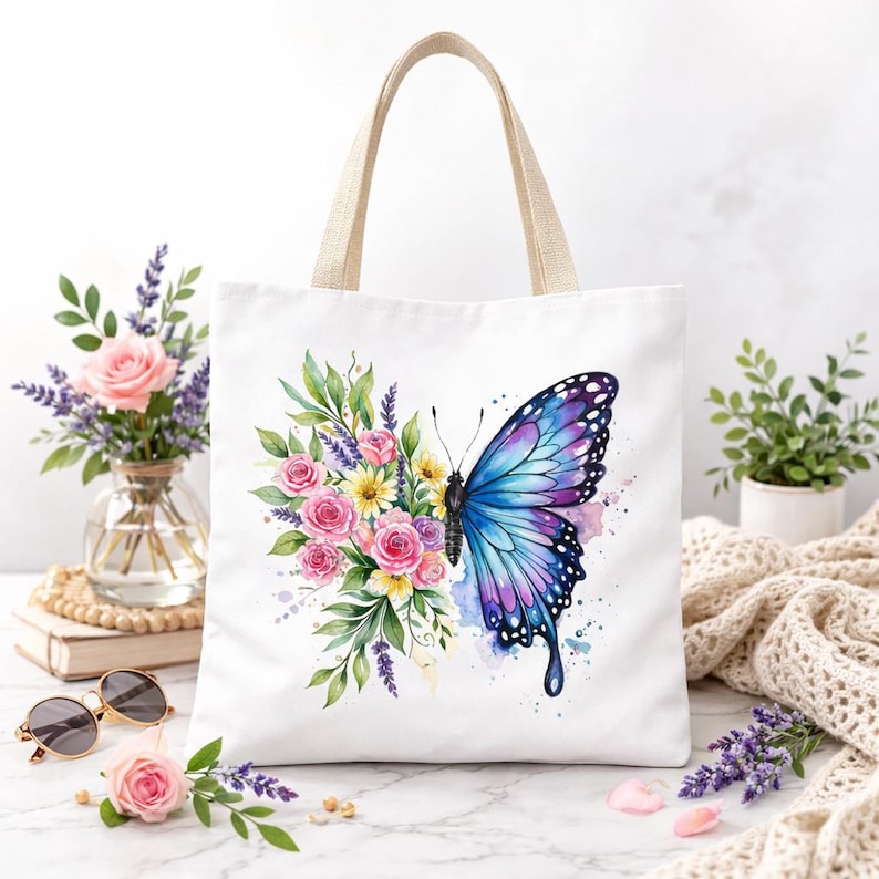 May include: White tote bag with a watercolor design of a blue and purple butterfly and a bouquet of pink and yellow flowers. The bag has beige handles and is sitting on a white surface.