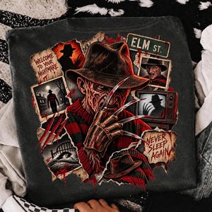 May include: A charcoal gray t-shirt featuring a graphic print of Freddy Krueger with a clawed glove, wearing a fedora and red and black striped sweater. The design includes text reading Welcome to your nightmare, Elm St., and Never sleep again.