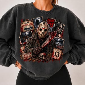 May include: A charcoal grey crewneck sweatshirt featuring a graphic print of a hockey-masked figure holding a machete. The design includes text reading Camp Crystal Lake, Friday the 13th, Kill Them All, and October 13, alongside imagery of a skull and lake.