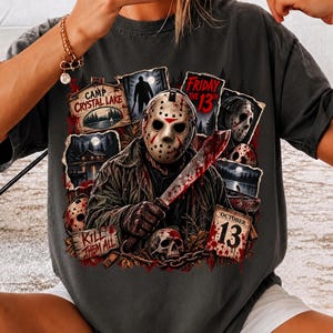 May include: A charcoal gray t-shirt featuring a graphic print of a hockey-masked figure holding a machete. The design includes text reading Camp Crystal Lake, Friday the 13th, Kill Them All, and October 13, alongside images of a skull and forest.