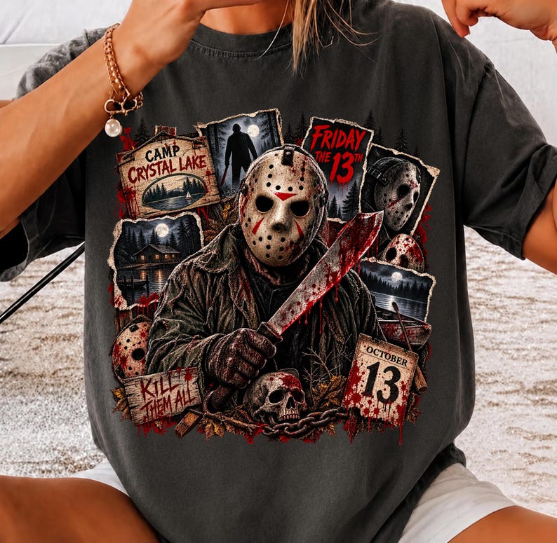 May include: A charcoal gray t-shirt featuring a graphic print of a hockey-masked figure holding a machete. The design includes text reading Camp Crystal Lake, Friday the 13th, Kill Them All, and October 13, alongside images of a skull and forest.
