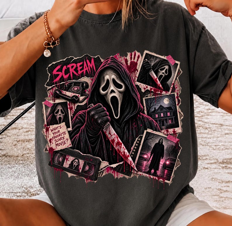 May include: A charcoal gray t-shirt featuring a graphic print of the Ghostface character from Scream. The design includes the text "SCREAM" and "WHAT'S YOUR FAVORITE SCARY MOVIE?" along with images of a telephone, a VHS tape, and scenes from the film.
