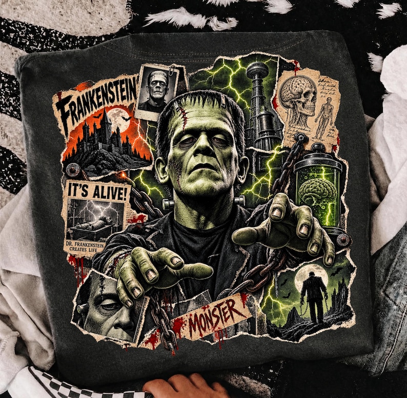 May include: A charcoal gray t-shirt featuring a graphic print of Frankenstein's monster with outstretched hands and chains. The design includes text reading Frankenstein, It's Alive, and Monster, alongside imagery of a castle, a brain in a jar, and a skull.