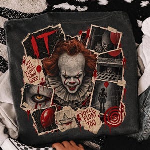 Op de afbeelding: Een antracietgrijs t-shirt met een collage van Pennywise de clown uit de film IT. De afbeelding bevat de tekst IT, We all float down here en You'll float too, samen met afbeeldingen van een rode ballon, een papieren bootje en een spiraal.