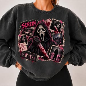 May include: A charcoal gray crewneck sweatshirt featuring a graphic print of the Ghostface character from the Scream movie franchise. The design includes a central figure holding a knife, a VHS tape, a rotary phone, and text reading Scream and What's Your Favorite Scary Movie?