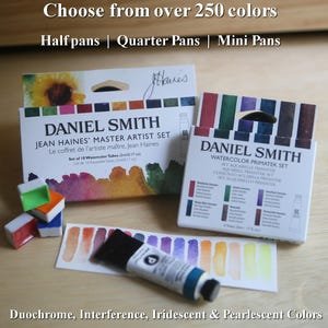 Puede incluir: Juegos de pintura de acuarela Daniel Smith. La imagen muestra dos cajas de pinturas de acuarela, un tubo de pintura y varias muestras de color. El texto en las cajas dice "Jean Haines' Master Artist Set" y "Watercolor Primatek Set". La imagen también incluye el texto "Elige entre más de 250 colores".