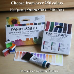 Puede incluir: Se muestran juegos de pintura de acuarela Daniel Smith. Las cajas son blancas con detalles coloridos y texto. El texto dice "Elige entre más de 250 colores" y "PrimaTek / Colores genuinos". También se ve un tubo de pintura azul y muestras de color.