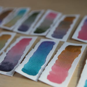 Swatches of the Da Vinci Tropical Palette which includes 6 half pans of the following colors: Sage & Amber, Joyce's Mother Violet, Denise's New Green, Artemis, Seaglass, Da Vinci Red Tint