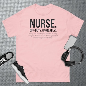 May include: A light pink t-shirt with the word "NURSE" in bold black letters. Below it, the text reads "OFF-DUTY. (PROBABLY)." A quote about self-care is printed below. Black sneakers, headphones, and a phone are also in the image.